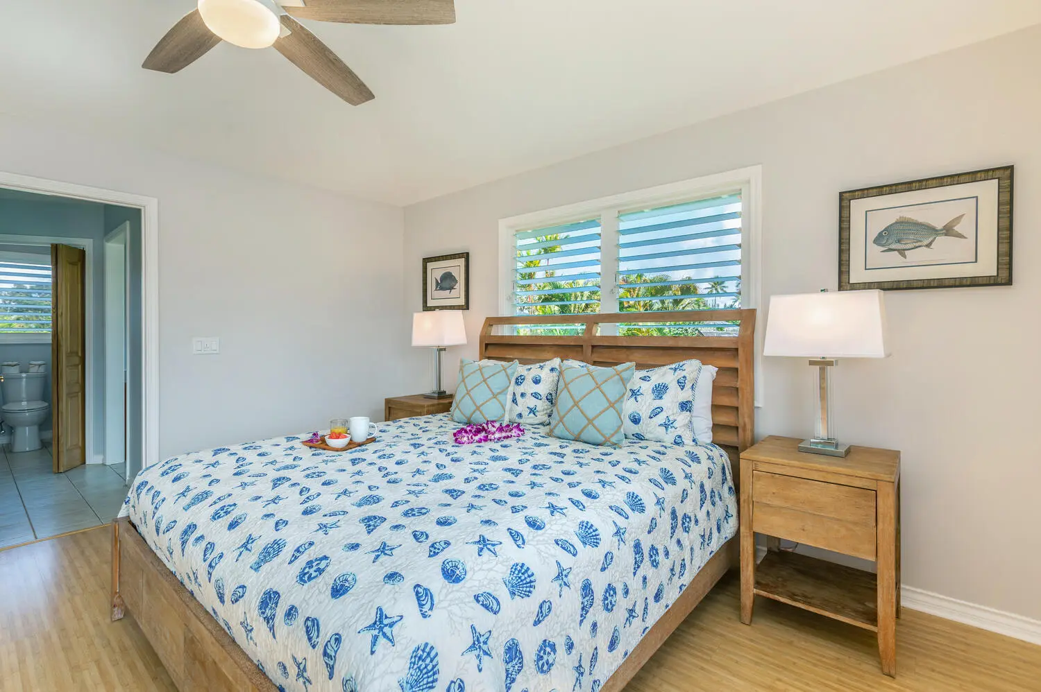 Lani Hanalei Suite. The wood bed with the blue shell-patterned quilt and fish prints, and an open doorway into the bathroom where a toilet and vanity are visible.