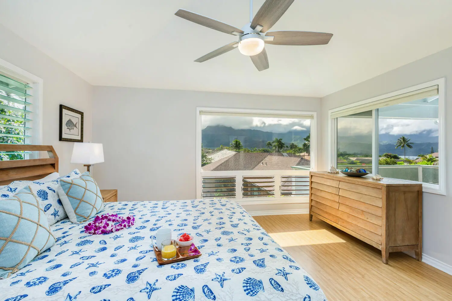 Lani Hanalei Suite. The shell-patterned bed in the foreground and a long wood dresser, with windows looking out to mountains, palms, and neighboring rooftops.